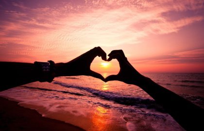 Hands making a heart shape around a sun setting