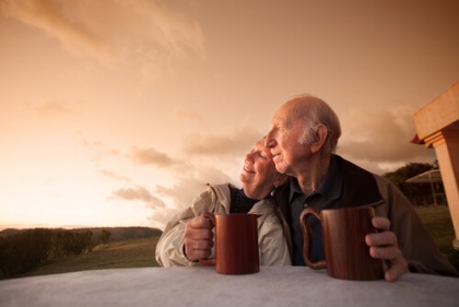Older couple watching sunrise or sunset with mugs