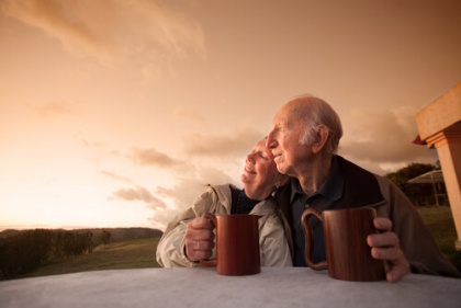 Older couple watching sunrise or sunset with mugs 