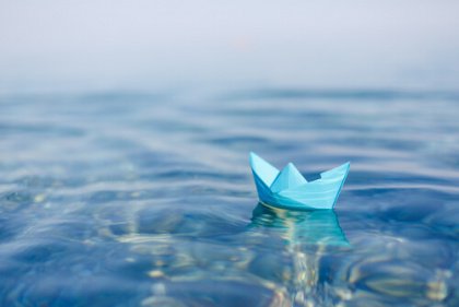 Small blue paper boat floating on water 