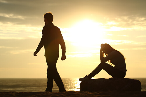 girl sitting on rock man walking on beach