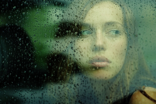 woman looking through glass with droplets of rain