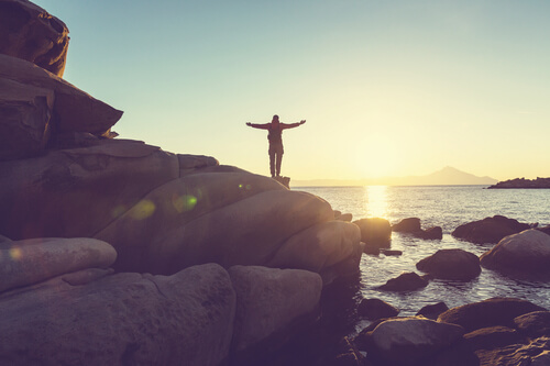 man with his arms open raised towards a mountain