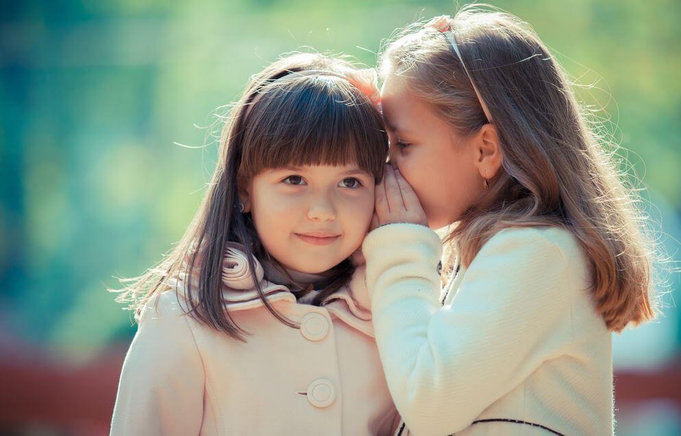small girl whispering secret to her friend
