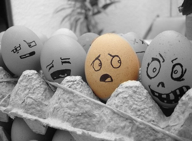A carton of eggs has silly faces drawn on them.