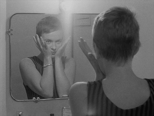 Gif of a woman playing peek-a-boo in the mirror.