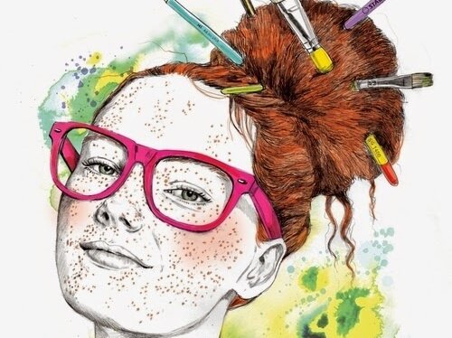 A girl with many freckles has paint brushes in her red hair.
