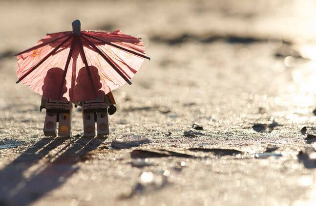 A lego couple is under a pink umbrella.