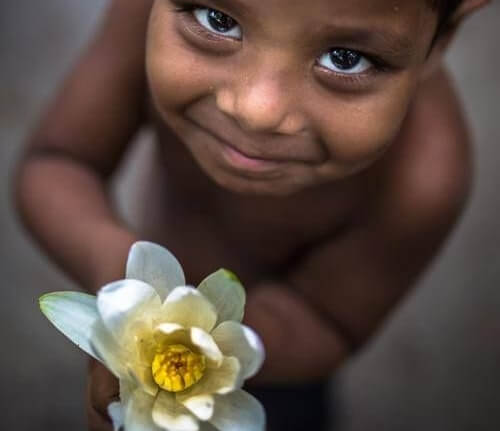 a grateful boy smiling and holding a flower