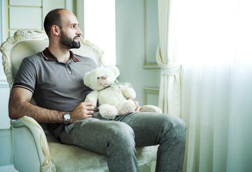 man holding a teddy bear looking out the window