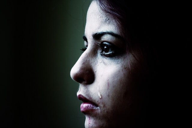 A sad girl has a tear drop falling down her cheek.