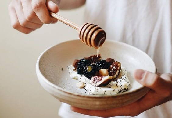 someone holding a dish with berries and honey