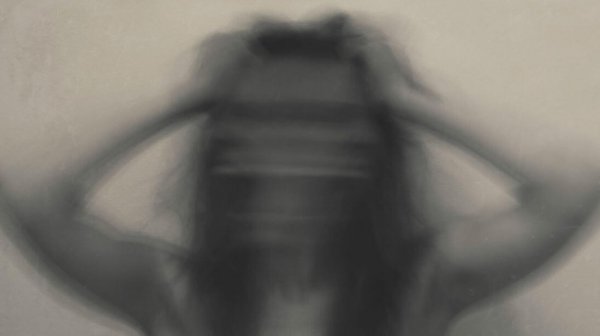  a blurry woman with her hands to her head in anxiety