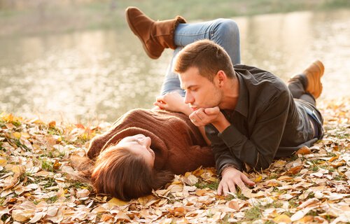 A couple in a new relationship laying in fall leaves next to a lake.