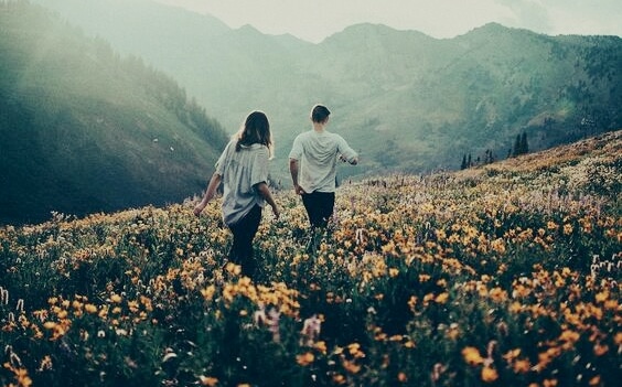 two people hiking in a mountain hill filled with flowers