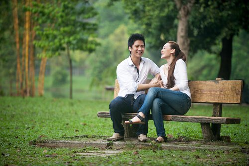 A couple is laughing on a park bench.