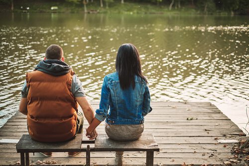 A couple is sitting in front of a lake holding hands.