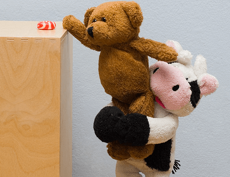 A stuffed cow is helping a stuffed bear reach something.