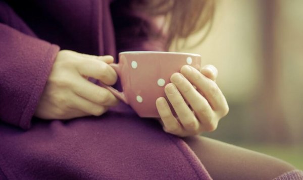 a woman holding a mug wearing a purple coat