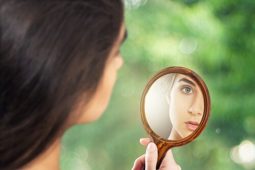 A woman looking at herself in a hand mirror.