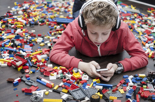 a little boy surrounded by toys but playing on a mobile device