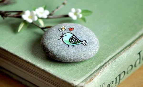 A bird carrying a flower, painted on a stone.