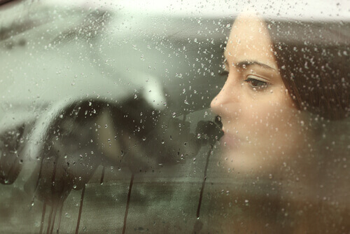 A sad woman inside a rainy car window.