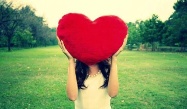 A woman holding a big, red heart over her head.