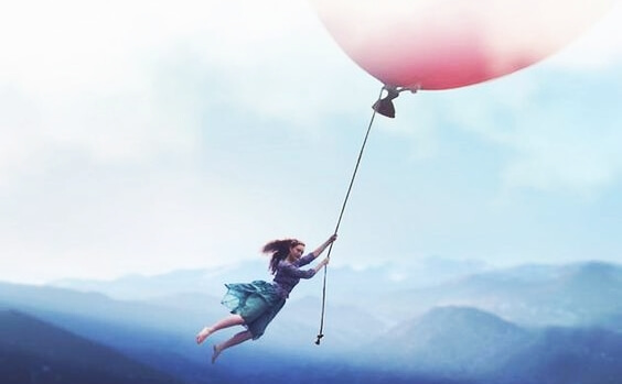 a girl holding on to a giant balloon over the mountains