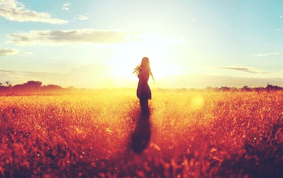 a woman standing in front of a bright sun in a field