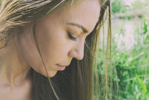 A woman looking down outside in the sun.