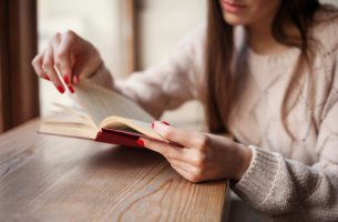 A woman with red nails is reading a book about heartbreak