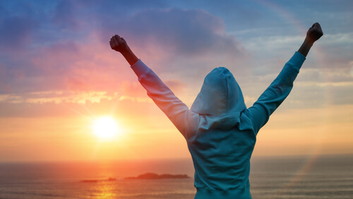 A woman with outstretched arms looking at the sea.