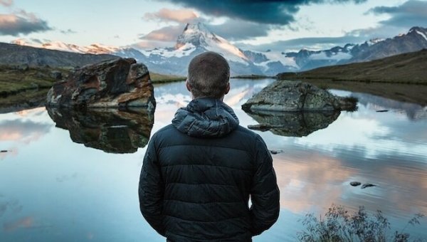 A man looking out at a mountain lake, reflecting and contemplating.