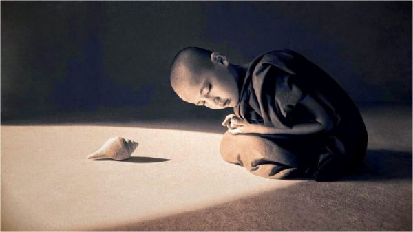 A boy praying next to a seashell in the sunlight.