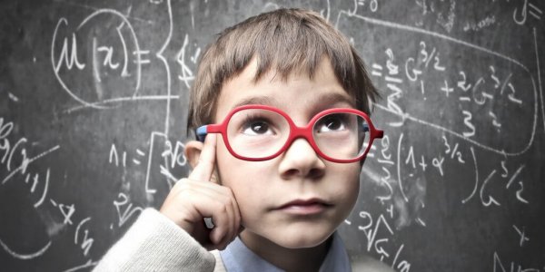 A young student wearing glasses thinking at a chalkboard full of math equations.