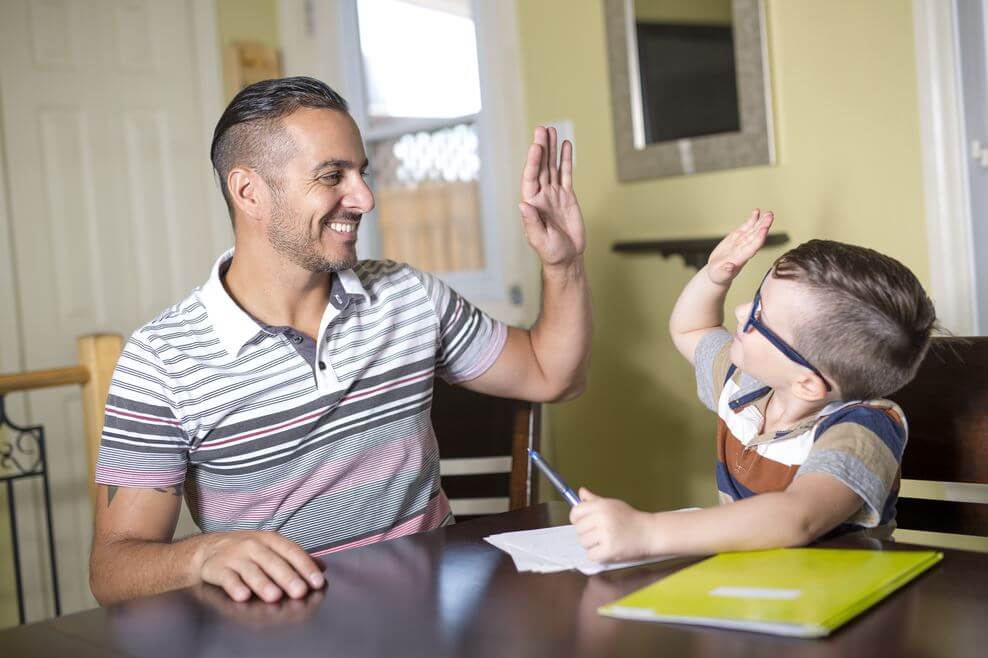 Father and son are highfiving while doing a homework assignment.