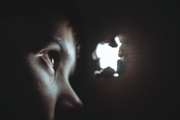 A child looking out of a hole in a dark box.