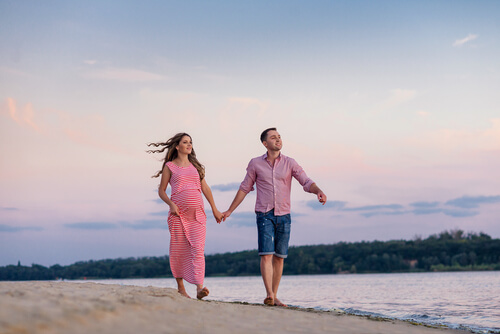 Pregnant woman and her husband walking along the beach.