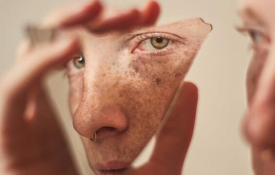 A woman looking at herself in a broken mirror.