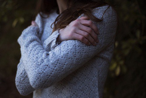 Woman in a sweater hugging self.