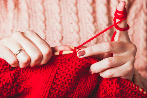 A woman knitting with red yarn.