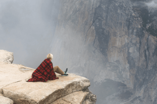 A woman is sitting at the edge of a cliff.