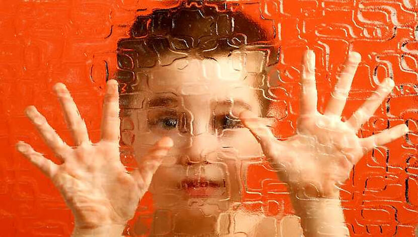A boy is pressing his palms against a distorted glass.