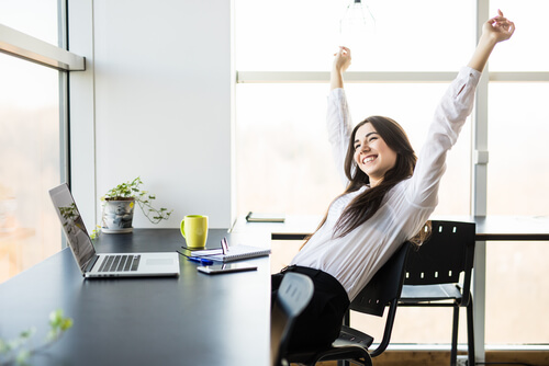 A happy woman stretching at her work desk.