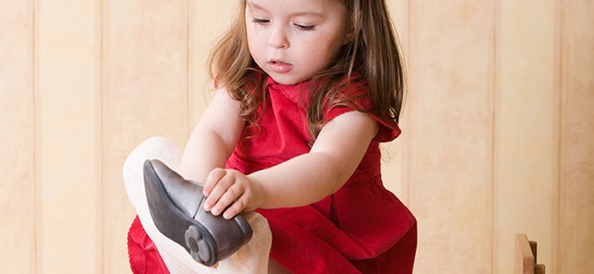 A little girl is putting on her shoe.