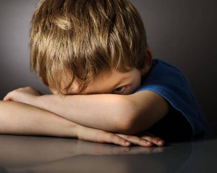 A boy is peeking out from over his crossed arm, with childhood schizophrenia