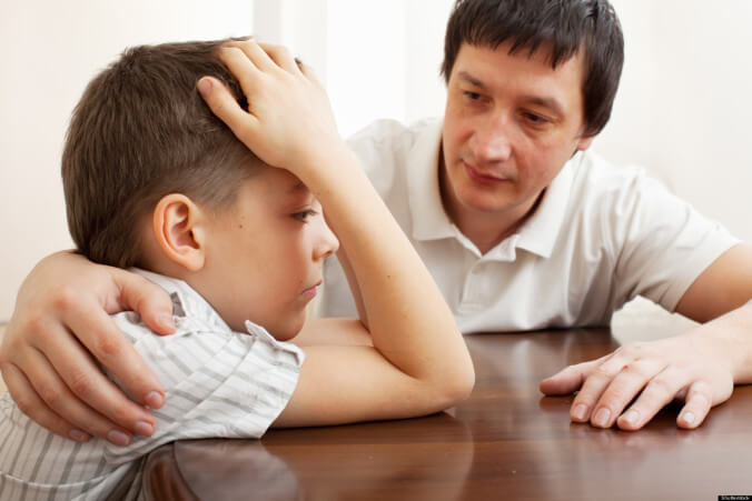 A father is putting his arm around his troubled son.