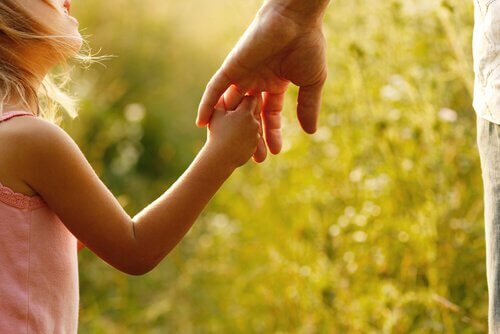 A girl is holding her fathers hand.