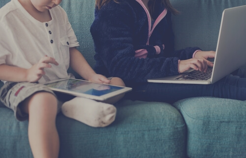 Two children with technology, one with a tablet and the other with a laptop.